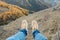 Person sits swinging legs on high cliff above green valley