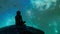 A person sits on a virtual rock their silhouette fading into the shimmering blue and green hues of the digital ocean