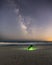 A person sitting alone on the beach under the Milky Way stretching across a dark sky.