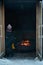 Person sitting in a wooden hut next to a campfire and warming up. Hut\\\'s doors are open and flames in the campfire burn