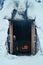Person sitting in a wooden hut next to a campfire and warming up. Hut\\\'s doors are open and flames in the campfire burn