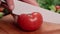 person slicing a tomato on a wooden board.