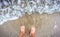 Person standing in ocean sea waves on sandy beach.