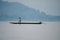 Person standing on the sea kayak on the water with mountains in the background