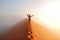 Person standing on top of dune in desert and looking at rising sun in mist with hands up, travel in Africa