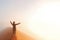 Person standing on top of dune in desert and looking at rising sun in mist with hands up, travel in Africa