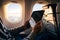 Person uses tablet in airplane, sunlit by window, for travel entertainment or work.