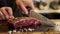 A person is using a knife to cut a piece of meat into smaller pieces on a cutting board