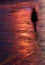 Person walking alone in the dark under bright orange light after rain