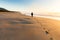 A person walking on a beautiful beach leaves a trail of footprints as the golden sunrise illuminates mist rising from the sea