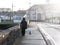 Person walking with dog on a foot path in a street at sunrise. Sun flare. Small town buildings in the background. Kilkee town,