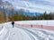Person walking on marked snow mobile trail along snow fence with walking stick