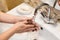 Person washing hands under water stream in bathroom sink, a stainless faucet