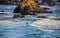 Person in wetsuit surfs past huge jutting rocks in Pacifice Northwest of USA in late afternoon