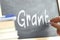 A person writing the word Grant on a blackboard.