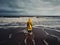 A person in a yellow raincoat standing on a beach. AI generative image.