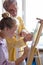 Personal art teacher teach little girl to draw on easel