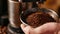 A persons hand holding a handful of brown aromatic coffee grounds freshly ground in a manual grinder