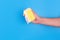 Persons hand holding yellow sponge for dish wash. Washcloth covered in soap. Domestic chores and supplies concept. Sensitive