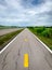 Perspective cracked asphalt road ahead to the mountain. Long straight damaged asphalt road. Bad surface of bike lane and white sky