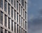 Perspective detail of tall high rise modern apartment building with geometric metallic cladding and dark windows next to