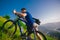 Perspective of a fit mountain biker pushing his bike uphill with amazing view on a forest, river and mountains in the background.