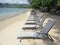 Perspective view of empty sun loungers on tropical beach with turquoise Caribbean sea. Row of empty deckchairs on the shore in the