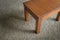 Perspective view of small teak table on beige carpet.