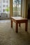 Perspective view of small teak table on carpet with balcony background.