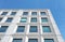 Perspective view of a white concrete office building against a bright blue sky with geometric brutalist 1960s details