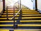 Perspective view of yellow stairs with silver metal handrail