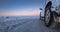 Perspective wheel of icy 4x4 car on a totally snowy road with tire tracks that goes all the way to the horizon with a purple and