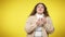 Perspiring overweight woman wiping face with tissue standing at yellow background. Portrait of smiling positive plus