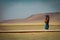 Peruvian woman in traditional clothing looks to cellphone, standing on a dry mountainous area