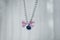 The pet necklace with blue bell and a pink bow with white stripes hanging from the top of the frame