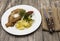 Petite Wiener schnitzel with boiled potatoes and ketchup. Served on a white porcelain plate with fork and knife on a wooden backgr