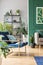 Petrol blue settee with pillow in living room with green wall, brown couch and urban jungle