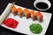 Philadelphia sushi rolls on a white square plate with wasabi, soy sauce and ginger. Dark wooden background
