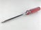 A Phillips-shaped screwdriver with a red plastic handle placed on a white surface.
