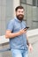 Phone for keeping in touch. Bearded man smile with mobile phone outdoors. Mobile phone messaging. Cell phone. Smartphone