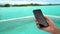 Phone screen closeup at pool. Woman holding cell phone smart phone screen near swimming pool