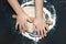 A photo from above of Kid`s hands, some flour, wheat dough and rolling-pin on the black table. Children hands kneading the rye do