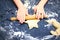 A photo from above of Kid`s hands, some flour, wheat dough and rolling-pin on the black table. Children hands kneading the star d