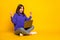 Photo of adorable lucky young lady dressed violet sweater sitting floor legs crossed typing device fists isolated yellow