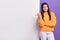 Photo of adorable pretty lady wear orange sweatshirt pointing thumb white wall empty space isolated violet color