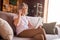 Photo of adorable pretty retired woman dressed white t-shirt sitting couch reading modern gadget smiling indoors flat