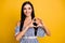 Photo of adorable shiny young lady wear striped dress showing heart fingers  yellow color background