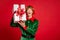Photo of amazed ginger elf hold gift open mouth amazed wear green x-mas costume headwear isolated red color background