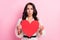 Photo of amazed nice young woman hold red paper heart shock news information  on pastel pink color background