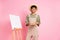 Photo of artist guy hold palette brush draw painting wear straw hat beige overall isolated pink color background